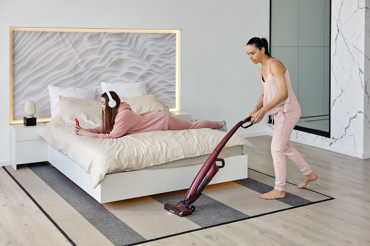 A person using the best cheap vacuum to clean a rug under a bed that has another person on it.