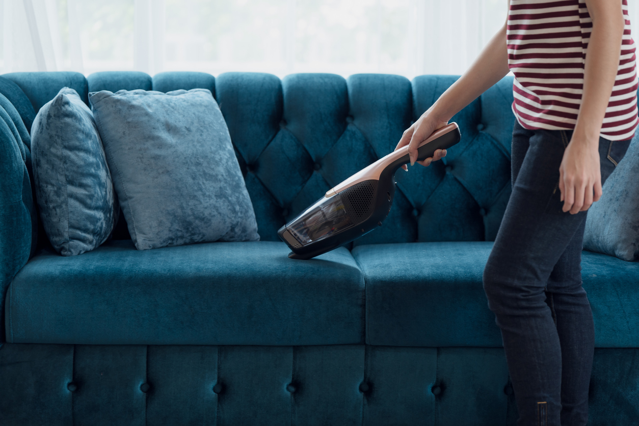 A person using the best cheap handheld vacuum to clean a blue couch.