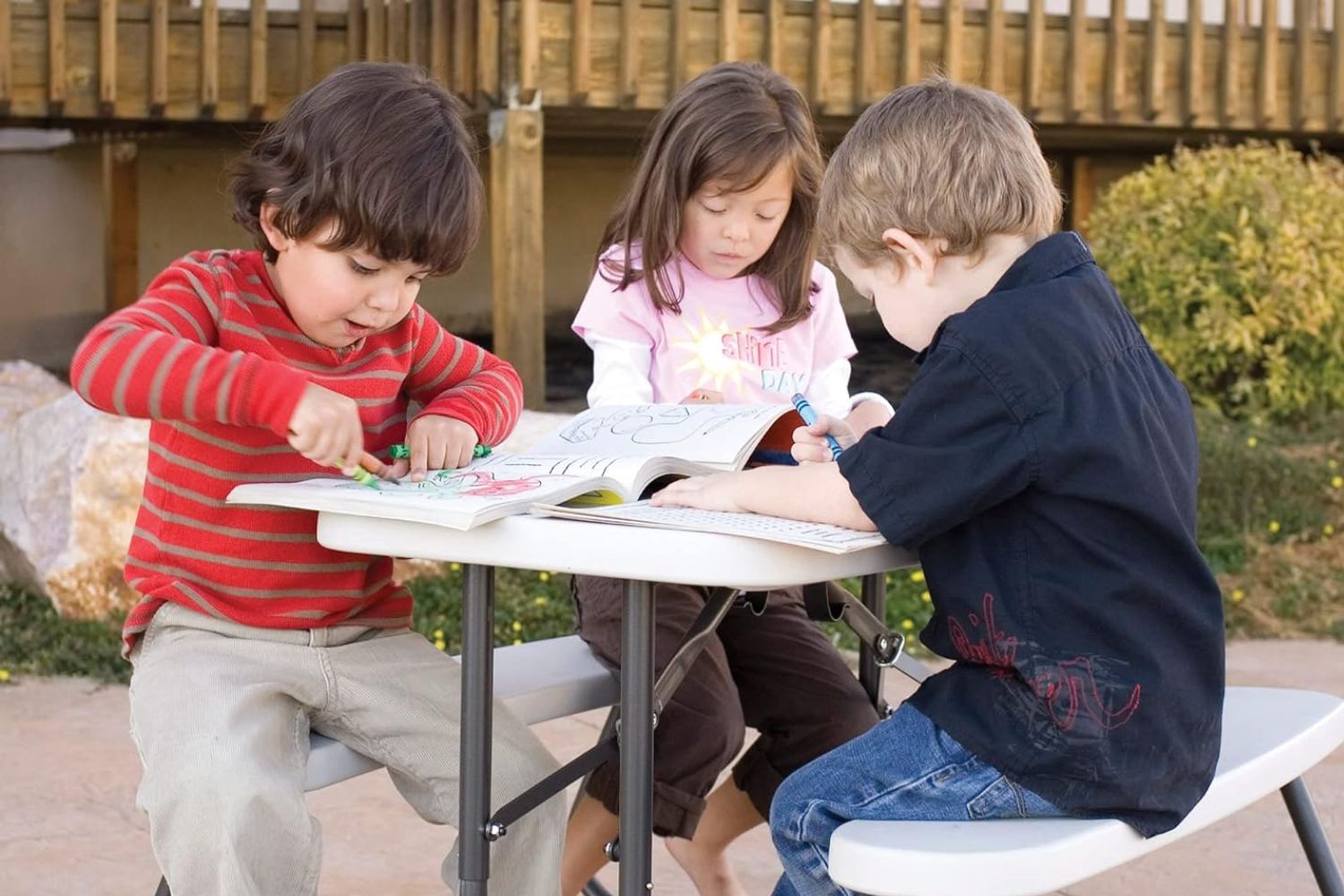 Three children coloring in books while sitting at the Lifetime Children’s Picnic Table.
